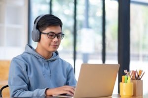 Young asian student man wearing headset and looking laptop display for learning online course from