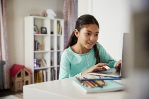 Young Girl Sitting At Desk In Bedroom Using Laptop To Do Homework